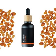 Schwarze Glasflasche mit Holzverschluss, die ätherisches Bio-Weihrauch-Öl enthält, umgeben von orangefarbenen Stücken Weihrauchhharz auf weißem Hintergrund